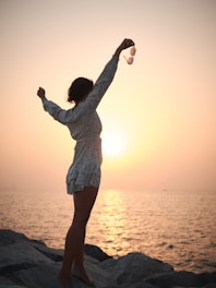 a woman standing on a rock with her arms in the air