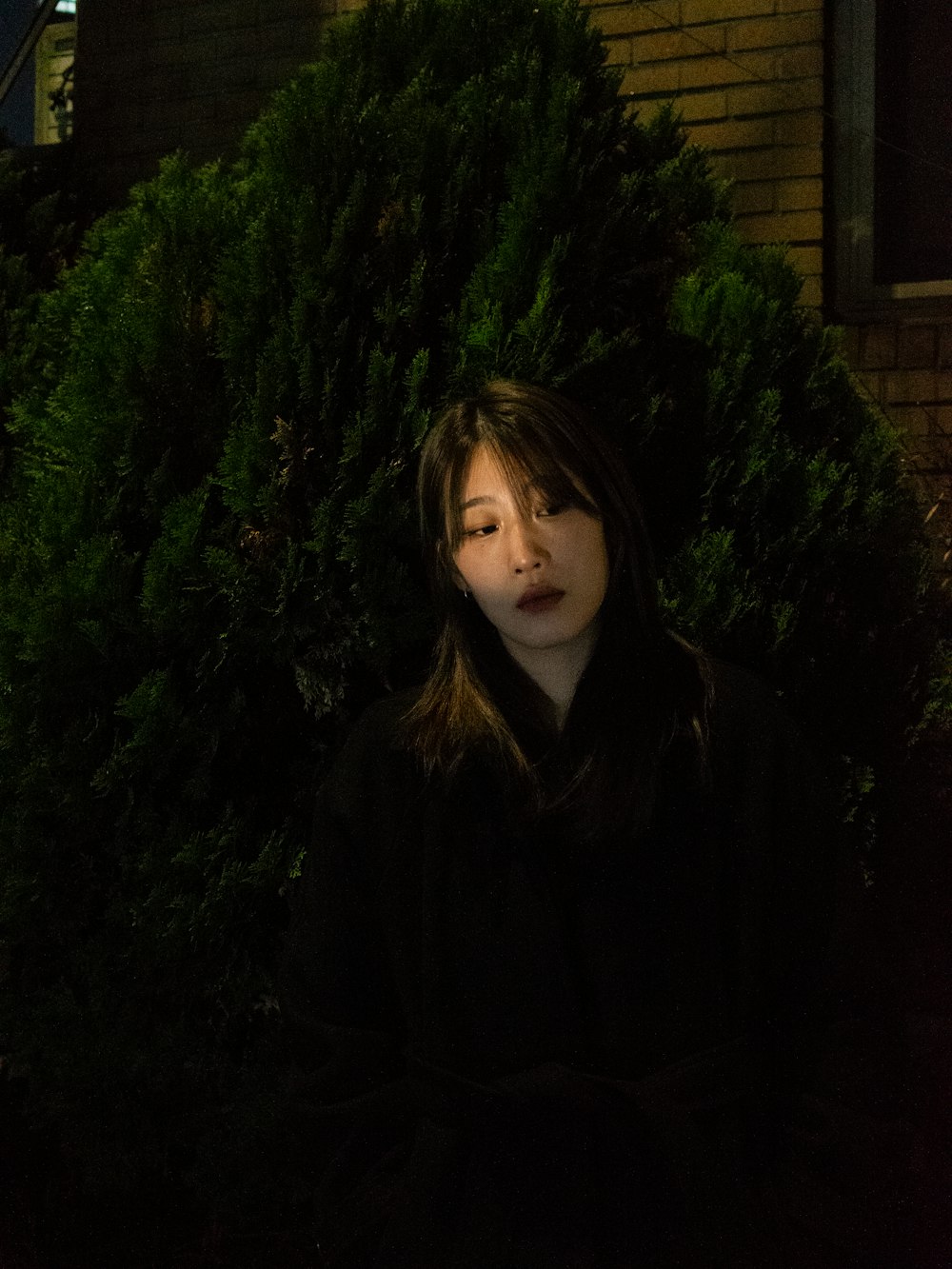 a woman sitting in front of a bush with her eyes closed