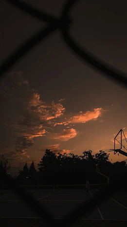 Sunset casting warm light over a packed basketball court with players mid-game.