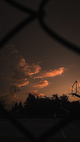 A basketball team huddled together on an outdoor court during sunset.