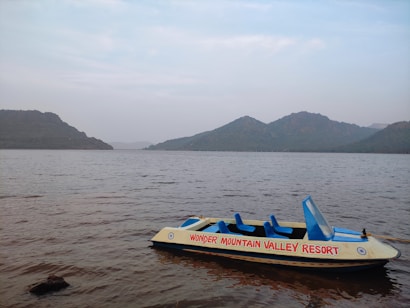 A small boat labeled 'Wonder Mountain Valley Resort' floats on a calm body of water, surrounded by distant green hills under a mostly cloudy sky.
