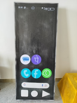 A large rectangular item resembling a smartphone screen is displayed, featuring various app icons on a dark background. The icons include popular social media and communication apps, arranged in a grid. The upper part shows symbols for time, battery, and network, while the lower portion has a navigation bar and app buttons.