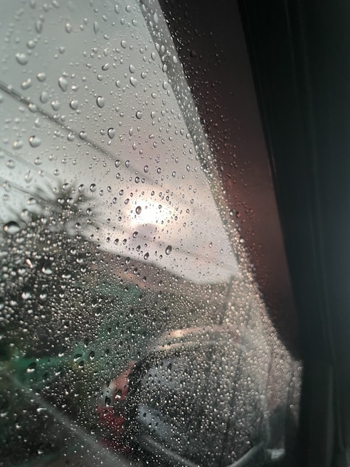 Gentle raindrops falling on a windowpane, blurring the view outside with a peaceful glow.