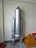 A model of a rocket made from metallic or aluminum-colored material stands upright. It has a central cylindrical body with two smaller cylindrical boosters attached to its sides. The rocket is positioned against a plain wall, and there is a pyramid-shaped structure with a brick-like pattern beside it.