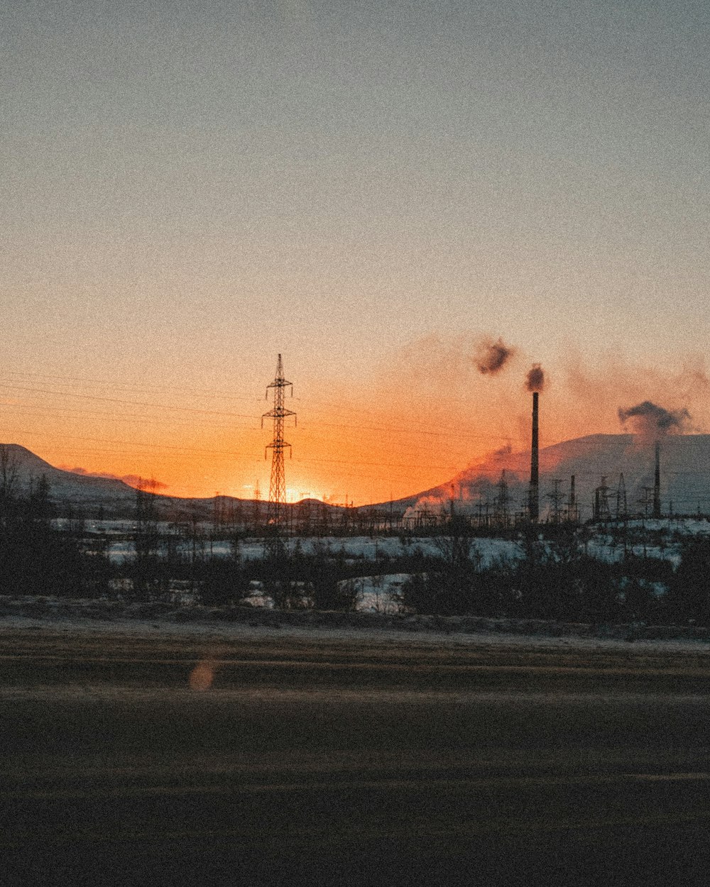 the sun is setting behind a factory with smoke stacks