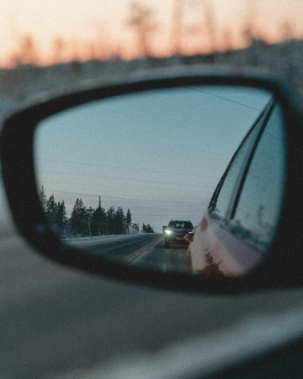 a car's side view mirror reflecting a car driving down the road