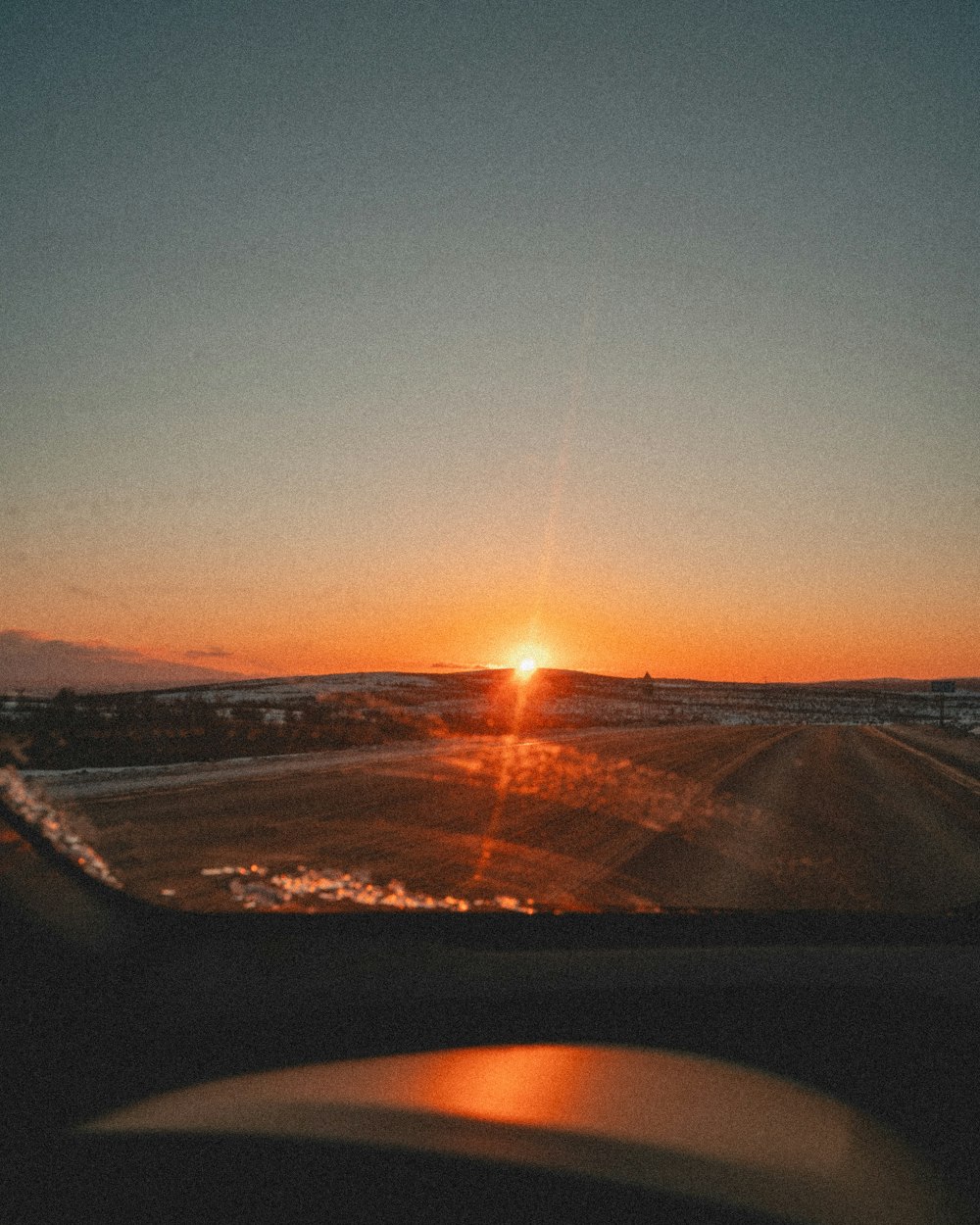 the sun is setting on a road near a field