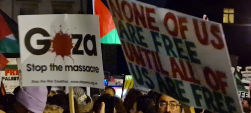 A crowd holding various protest signs with bold messages, including advocacy for Gaza and a call for solidarity and freedom.