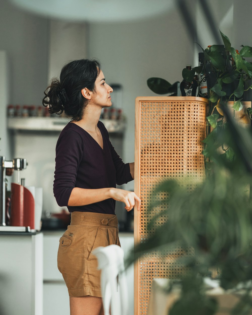 a woman standing next to a plant in a kitchen