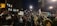 A large group of people gathered outdoors during the night, many of whom are holding various signs and banners. Some of the signs read 'Free Palestine' and 'Gaza, stop the massacre.' The crowd is densely packed, with many individuals wearing winter clothing such as jackets and hats.