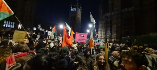 A powerful crowd waving flags at a lively political rally during sunset.