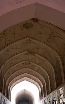 An architectural interior view featuring a series of ornate, arched ceilings with decorative patterns. The design includes geometric motifs and a symmetrical layout, highlighting sophisticated craftsmanship. Light filters through the space, creating a contrast between the illuminated arches and the darker, richly detailed sections.