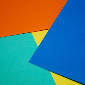 Various colored sheets of paper, including orange, blue, yellow, and teal, overlap each other at different angles.