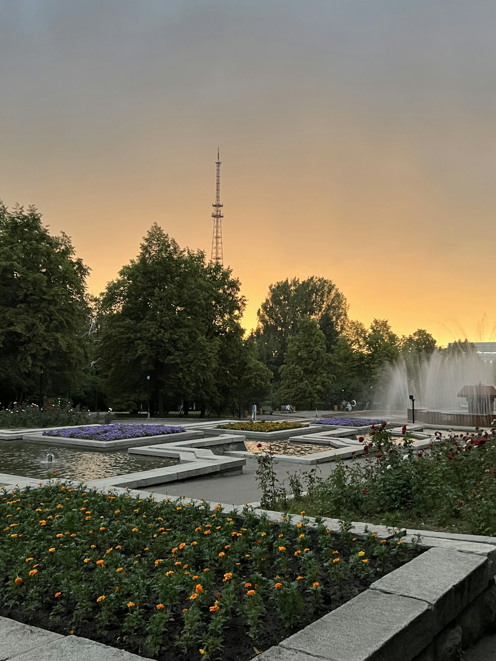 a park with a fountain and flowers in the foreground