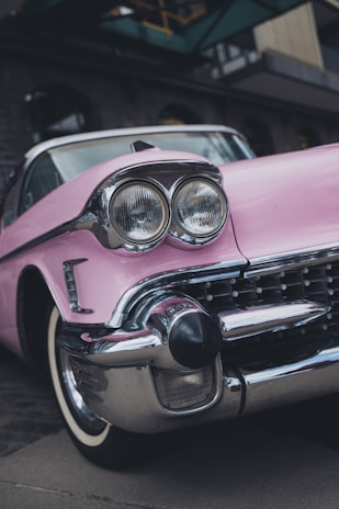 A vintage car with a distinctive pink color and chrome details, featuring large round headlights and a classic design.
