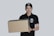 A person wearing a black cap and a black polo shirt with a courier service logo holds a large cardboard box. The background is a plain light gray, and the person appears to be smiling slightly.