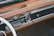 A vintage car dashboard featuring a classic radio with tuning dials and buttons. The dashboard is made of brown leather and wood, with a smooth and polished finish. The design includes chrome accents and an analog clock.