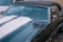 A classic convertible car with a black soft-top roof and glossy paint featuring bold white racing stripes on the hood. The car is parked on a cobblestone street next to a white vehicle.