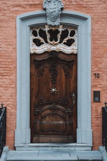 Elegant wrought iron door with a brushed bronze finish, set against a textured stone wall.