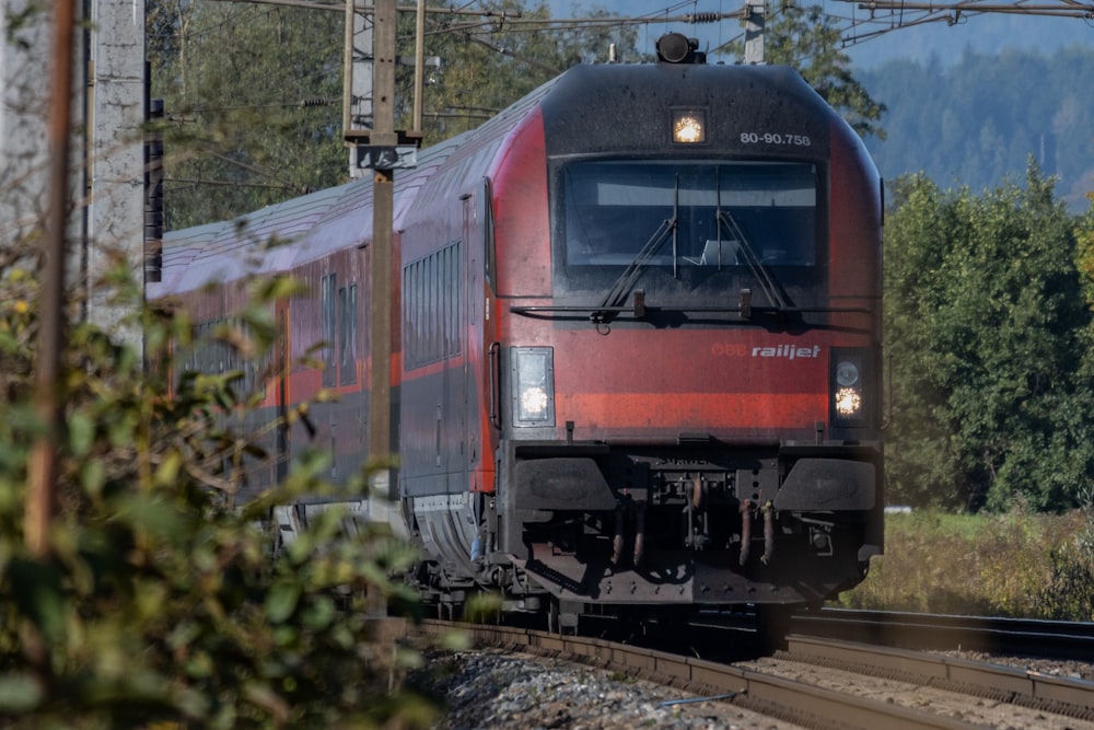 a red train traveling down train tracks next to a forest