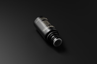 A sleek black bottle with gold accents resting on a dark charcoal surface, softly lit to highlight its minimalist design.