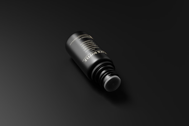 A sleek black bottle is positioned against a dark background. The bottle has elegant gold text on its surface, reflecting a minimalist and luxurious design.
