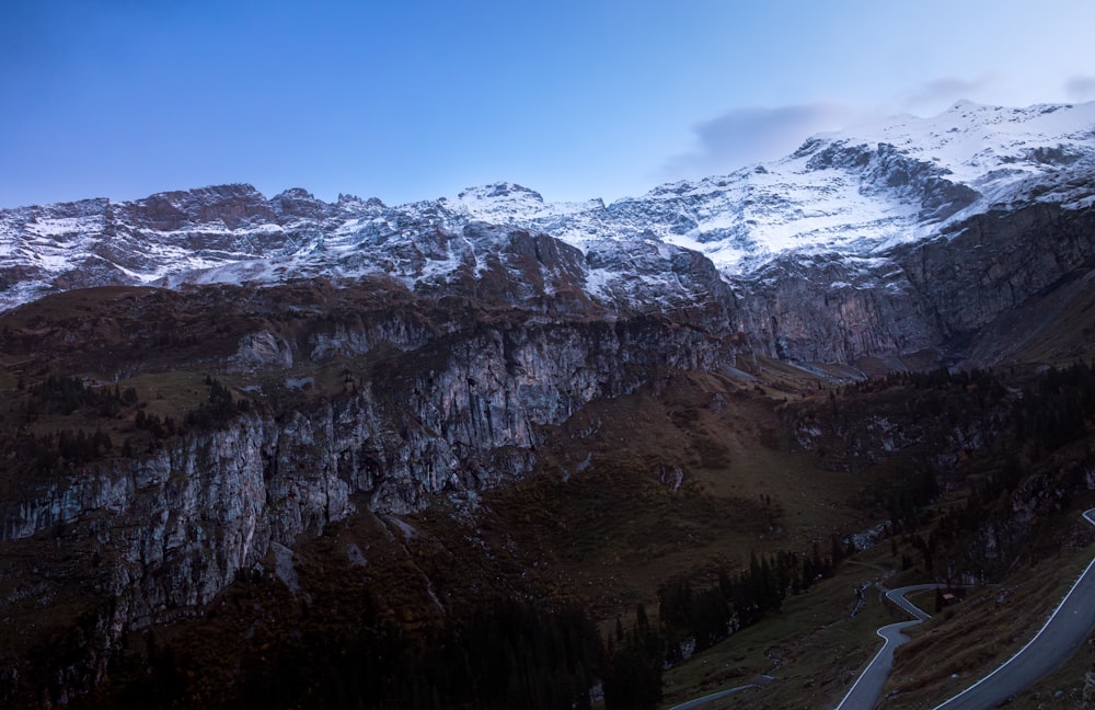 a winding road in the mountains with snow on the top