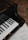 A close-up view of a sleek, black grand piano keyboard. The keys are glossy and well-polished, reflecting light beautifully, with a background of a wooden floor and a subtle rug.