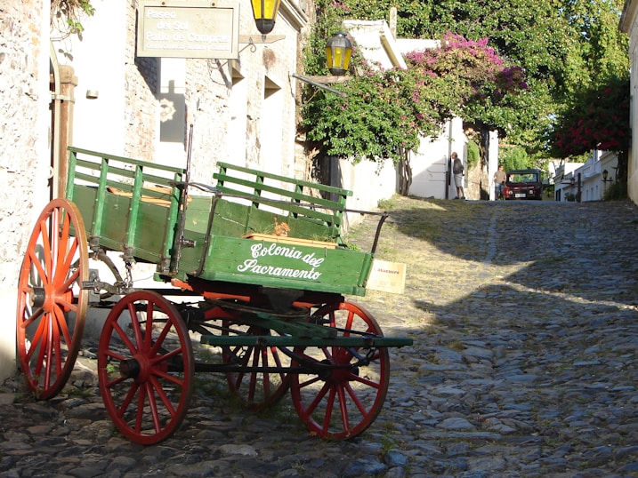 a green and red wagon sitting on a cobblestone street