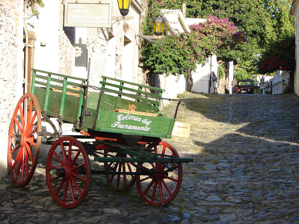 a green and red wagon sitting on a cobblestone street