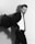 A man in a suit appears to be in motion, as if turning quickly. He has a serious expression and is dressed in a dark blazer, white shirt, and tie. The background is plain, and the image is in black and white, contributing to a dramatic and professional atmosphere.