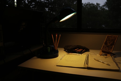 A quiet writer's desk with a notebook and pen beside a softly glowing lamp.