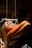 A rugged brown leather boot with laces is suspended in the air by a string. The sole of the boot is visible, highlighting its thick tread pattern. The background is dimly lit, creating focus on the boot.