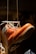 A rugged brown leather boot with laces is suspended in the air by a string. The sole of the boot is visible, highlighting its thick tread pattern. The background is dimly lit, creating focus on the boot.