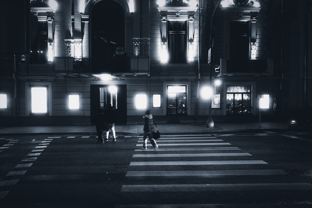 a couple of people walking across a street at night