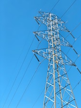 A towering metal electricity pylon stands against a clear blue sky. Several power lines extend from the structure, highlighting its function and connectivity.