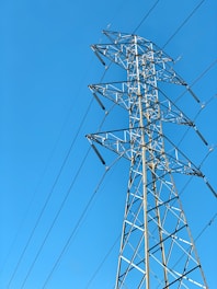 A towering metal electricity pylon stands against a clear blue sky. Several power lines extend from the structure, highlighting its function and connectivity.