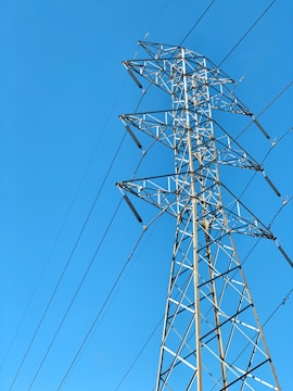 A towering metal electricity pylon stands against a clear blue sky. Several power lines extend from the structure, highlighting its function and connectivity.