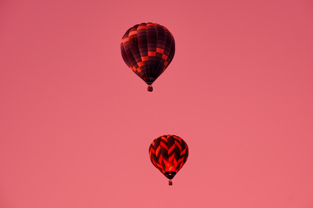 a couple of hot air balloons flying through a pink sky