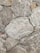Rough stone tiles are laid out in an uneven pattern. The surfaces feature white and beige veins running across various shades of gray and brown. The texture appears rugged and natural, with some stones having sharper edges, while others seem more rounded.