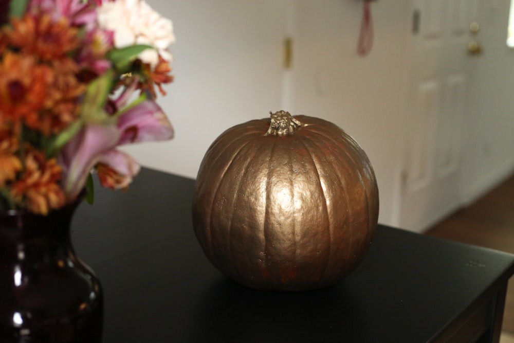a metallic pumpkin sitting on a table next to a vase of flowers