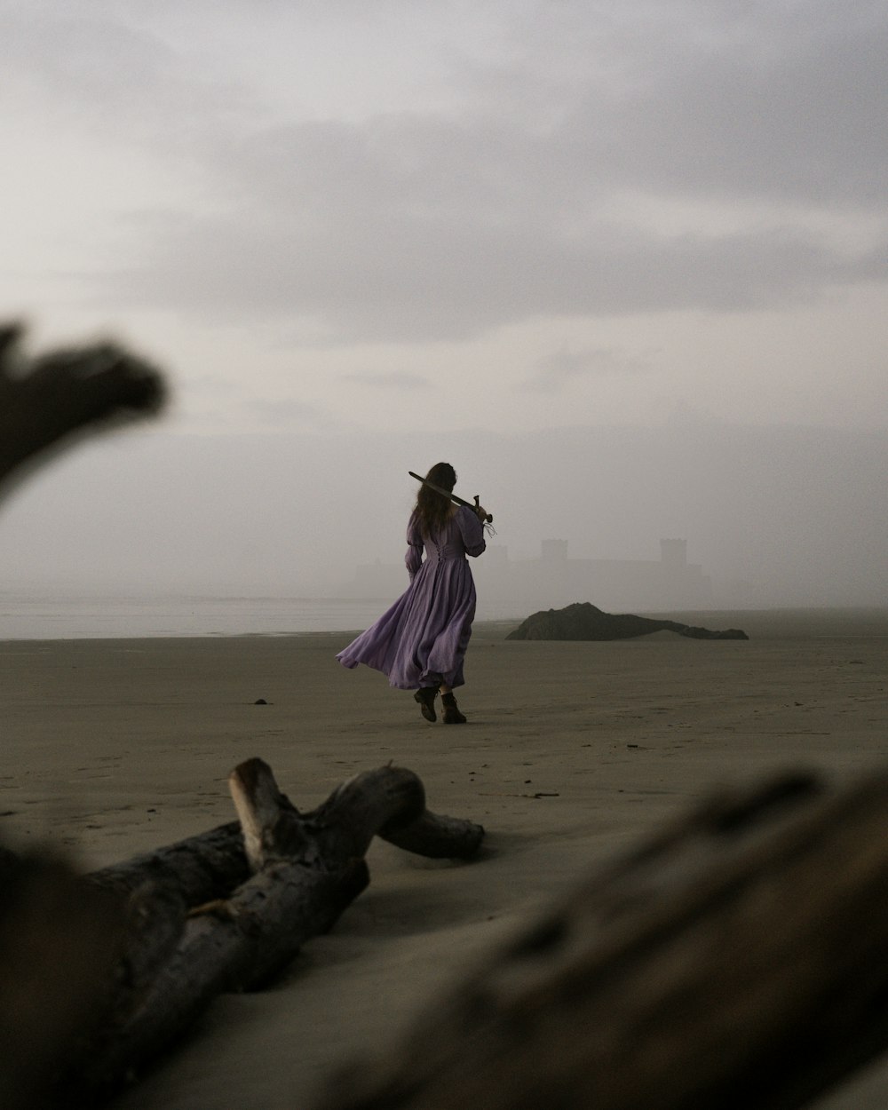 해변에 서 있는 긴 보라색 드레스를 입은 여자
