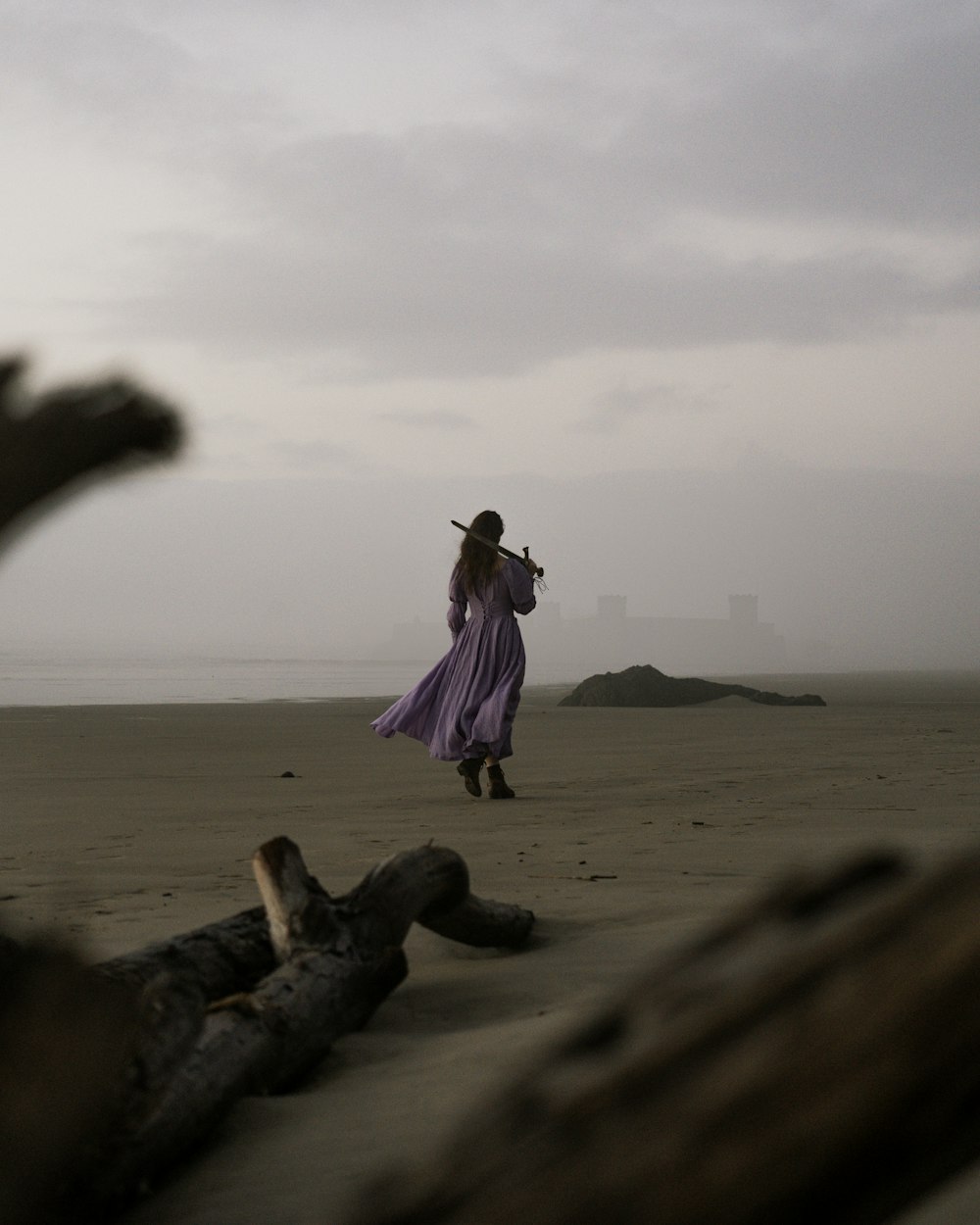 eine Frau in einem langen lila Kleid steht an einem Strand