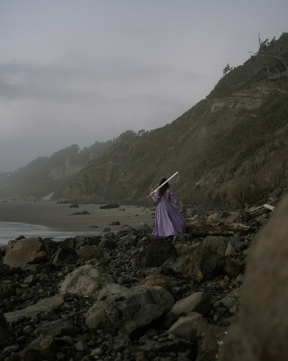 a woman in a purple dress is walking on a rocky beach