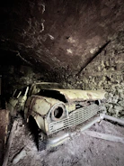 A junked car in a garage with a visible phone number painted on the wall.