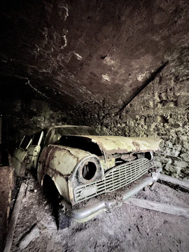 A junked car in a garage with a visible phone number painted on the wall.