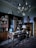 An elegant study room with an antique wooden desk and a vintage globe. The room includes a large wooden bookshelf filled with books, a decorative rug on the floor, and a chandelier hanging from the ceiling. A bust sits atop a tall wooden dresser, and an ornate lamp is placed on the desk.