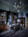 An elegant study room with an antique wooden desk and a vintage globe. The room includes a large wooden bookshelf filled with books, a decorative rug on the floor, and a chandelier hanging from the ceiling. A bust sits atop a tall wooden dresser, and an ornate lamp is placed on the desk.