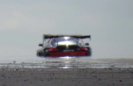 Low-angle view of a performance car’s suspension and wheel well in motion, with blurred asphalt and heat haze.