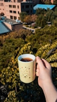 A close-up of hands holding a warm mug against a blurred cityscape background.